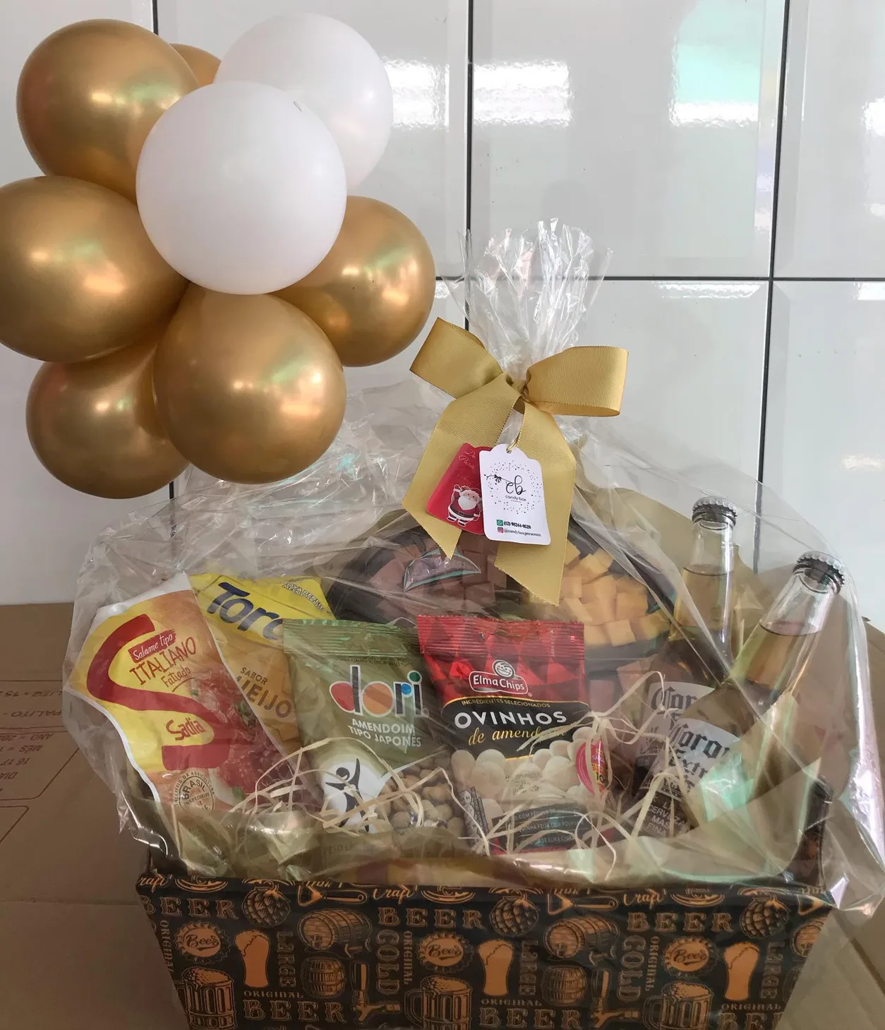 Cesta embrulhada em celofane com laço dourado e balões dourados e brancos